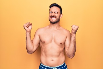 Fototapeta premium Young handsome man with beard wearing sleeveless t-shirt standing over yellow background very happy and excited doing winner gesture with arms raised, smiling and screaming for success. Celebration