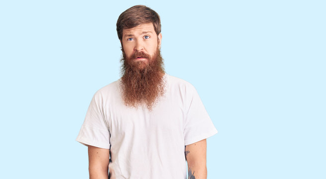 Handsome young red head man with long beard wearing casual white tshirt relaxed with serious expression on face. simple and natural looking at the camera.
