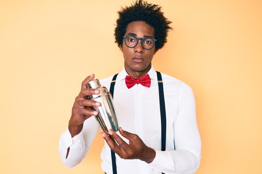 Handsome african american bartender man with afro hair preparing cocktail mixing drink with shaker relaxed with serious expression on face. simple and natural looking at the camera.