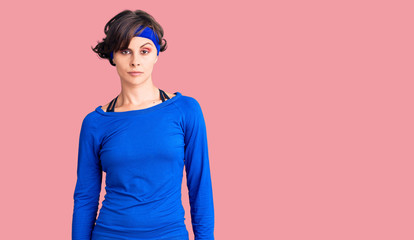 Beautiful young woman with short hair wearing training workout clothes skeptic and nervous,...
