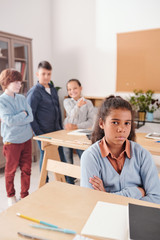 Offended schoolgirl on background of classmates laughing and bullying her