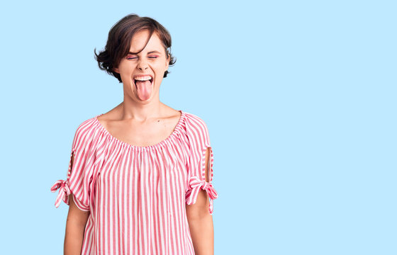 Beautiful young woman with short hair wearing casual summer clothes sticking tongue out happy with funny expression. emotion concept.