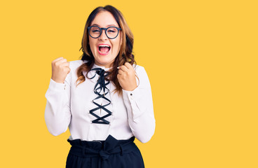 Young beautiful caucasian woman wearing business shirt and glasses screaming proud, celebrating victory and success very excited with raised arms