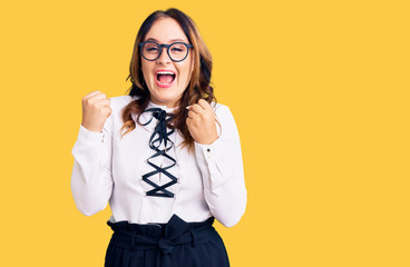 Young beautiful caucasian woman wearing business shirt and glasses screaming proud, celebrating...