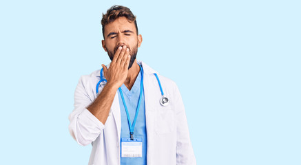 Young hispanic man wearing doctor uniform and stethoscope bored yawning tired covering mouth with hand. restless and sleepiness.