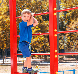 
Little blonde boy on a red children's sports climbing frame