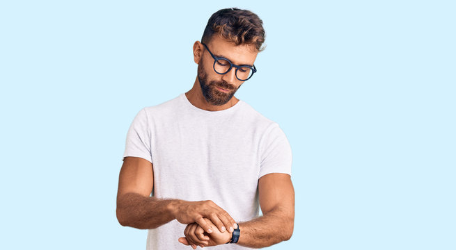 Young hispanic man wearing casual clothes and glasses checking the time on wrist watch, relaxed and confident
