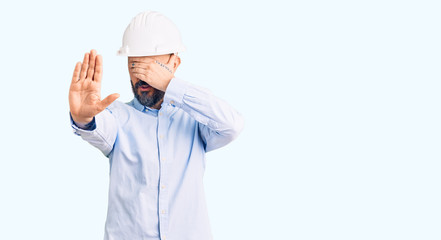 Young handsome man wearing architect hardhat covering eyes with hands and doing stop gesture with sad and fear expression. embarrassed and negative concept.