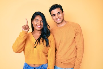Fototapeta premium Beautiful latin young couple wearing casual clothes together showing and pointing up with finger number one while smiling confident and happy.