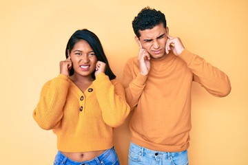 Beautiful latin young couple wearing casual clothes together covering ears with fingers with annoyed expression for the noise of loud music. deaf concept.