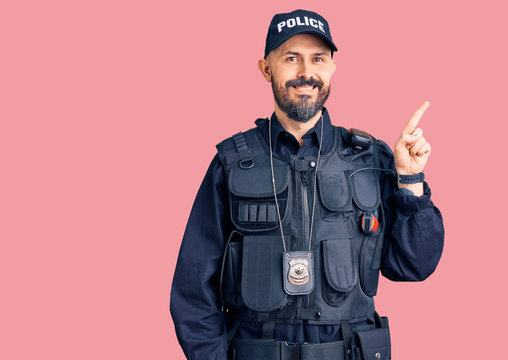 Young handsome man wearing police uniform with a big smile on face, pointing with hand finger to the side looking at the camera.
