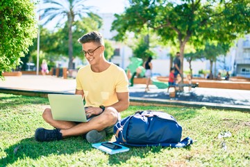 Obraz premium Young hispanic student smiling happy using laptop sitting on the grass at the university campus