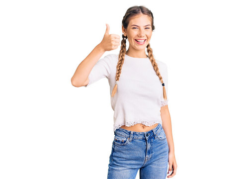 Beautiful caucasian woman with blonde hair wearing braids and white tshirt smiling happy and positive, thumb up doing excellent and approval sign
