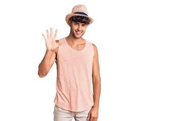 Young hispanic man wearing summer hat showing and pointing up with fingers number five while smiling confident and happy.