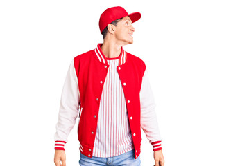 Young handsome man wearing baseball uniform looking away to side with smile on face, natural expression. laughing confident.