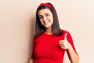 Young beautiful girl wearing casual t shirt and diadem doing happy thumbs up gesture with hand. approving expression looking at the camera showing success.