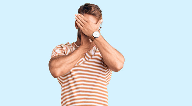 Young caucasian man wearing casual clothes and glasses covering eyes and mouth with hands, surprised and shocked. hiding emotion
