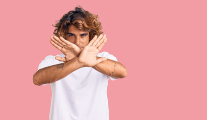 Young hispanic man wearing casual white tshirt rejection expression crossing arms doing negative sign, angry face