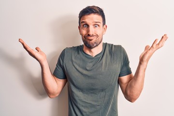 Young handsome man wearing casual t-shirt standing over isolated white background clueless and confused with open arms, no idea and doubtful face.