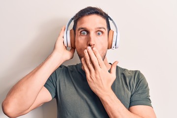 Young handsome man listening to music using headphones over isolated white background covering mouth with hand, shocked and afraid for mistake. Surprised expression