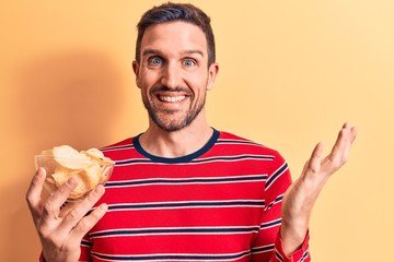 Young handsome man holding bowl of potato chips standing over isolated yellow background...