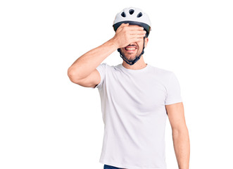 Young handsome man wearing bike helmet smiling and laughing with hand on face covering eyes for surprise. blind concept.
