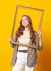 portrait of woman with empty picture art frame isolated on yellow background