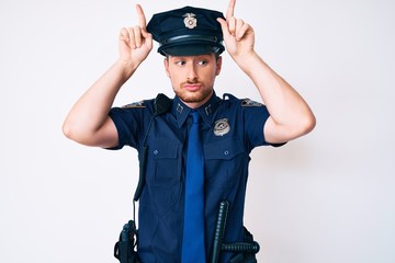 Young caucasian man wearing police uniform doing funny gesture with finger over head as bull horns