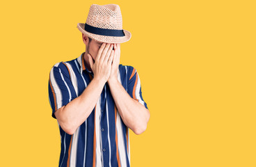 Young handsome caucasian man wearing summer hat with sad expression covering face with hands while crying. depression concept.