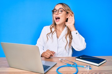 Young beautiful blonde woman wearing doctor uniform working at the clinic smiling with hand over ear listening and hearing to rumor or gossip. deafness concept.