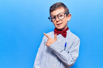 Cute blond kid wearing nerd bow tie and glasses cheerful with a smile of face pointing with hand...