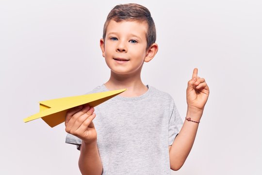 Cute blond kid holding paper airplane smiling happy pointing with hand and finger to the side