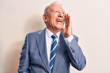 Senior handsome grey-haired businessman wearing elegant suit over white background shouting and screaming loud to side with hand on mouth. Communication concept.