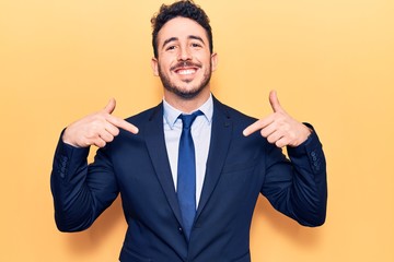 Young hispanic man wearing suit looking confident with smile on face, pointing oneself with fingers...
