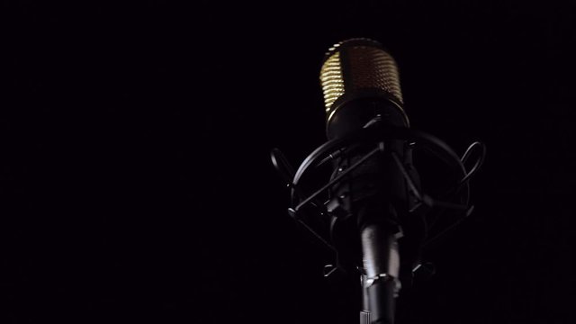 Micr&oacute;fono profesional de sobre mesa con cable y montado en su base con un fondo negro, e iluminaci&oacute;n en movimiento.