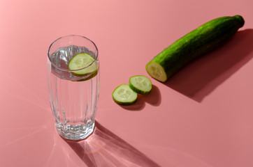 still life. Glittering glasses of cucumber water on pink table background in sunlight. Refreshment concept.
