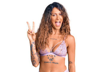 Young hispanic woman with tattoo wearing lingerie smiling looking to the camera showing fingers...