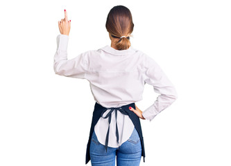 Beautiful brunette young woman wearing professional waitress apron posing backwards pointing ahead...