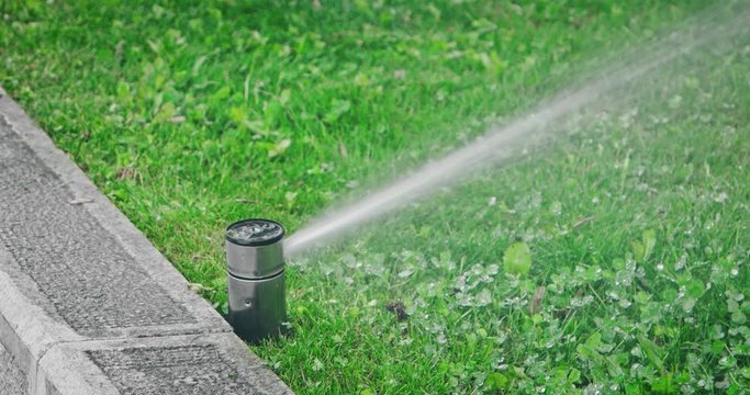Irrigation System. Automatic lawn sprinkler, watering a large green public park field. Grownd level view, loopable clip