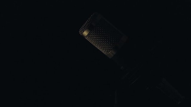Micr&oacute;fono profesional de sobre mesa con cable y montado en su base con un fondo negro, e iluminaci&oacute;n en movimiento.