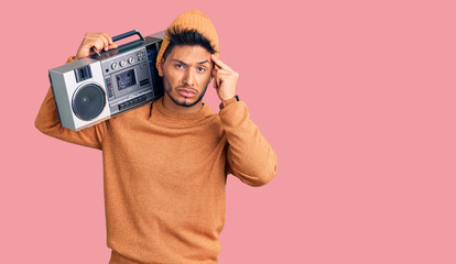 Handsome latin american young man holding boombox, listening to music worried and stressed about a problem with hand on forehead, nervous and anxious for crisis