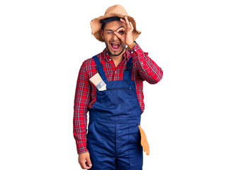 Handsome latin american young man weaing handyman uniform doing ok gesture with hand smiling, eye looking through fingers with happy face.