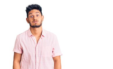 Handsome latin american young man wearing casual summer shirt puffing cheeks with funny face. mouth inflated with air, crazy expression.