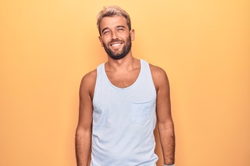 Young handsome blond man wearing casual sleeveless t-shirt over isolated yellow background with a happy and cool smile on face. Lucky person.