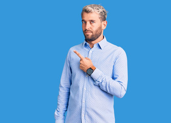 Young handsome blond man wearing elegant shirt pointing with hand finger to the side showing advertisement, serious and calm face