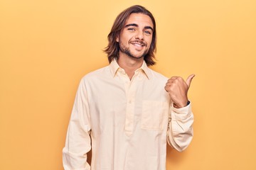 Young handsome man wearing business clothes smiling with happy face looking and pointing to the side with thumb up.