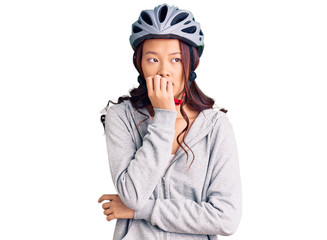 Young beautiful chinese girl wearing bike helmet looking stressed and nervous with hands on mouth biting nails. anxiety problem.