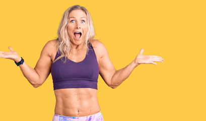 Middle age fit blonde woman wearing sportswear celebrating victory with happy smile and winner expression with raised hands