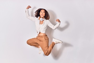 Young beautiful chinese woman smiling happy. Jumping with smile on face listening to music using...