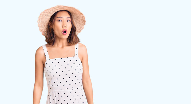 Young beautiful chinese girl wearing summer hat afraid and shocked with surprise expression, fear and excited face.